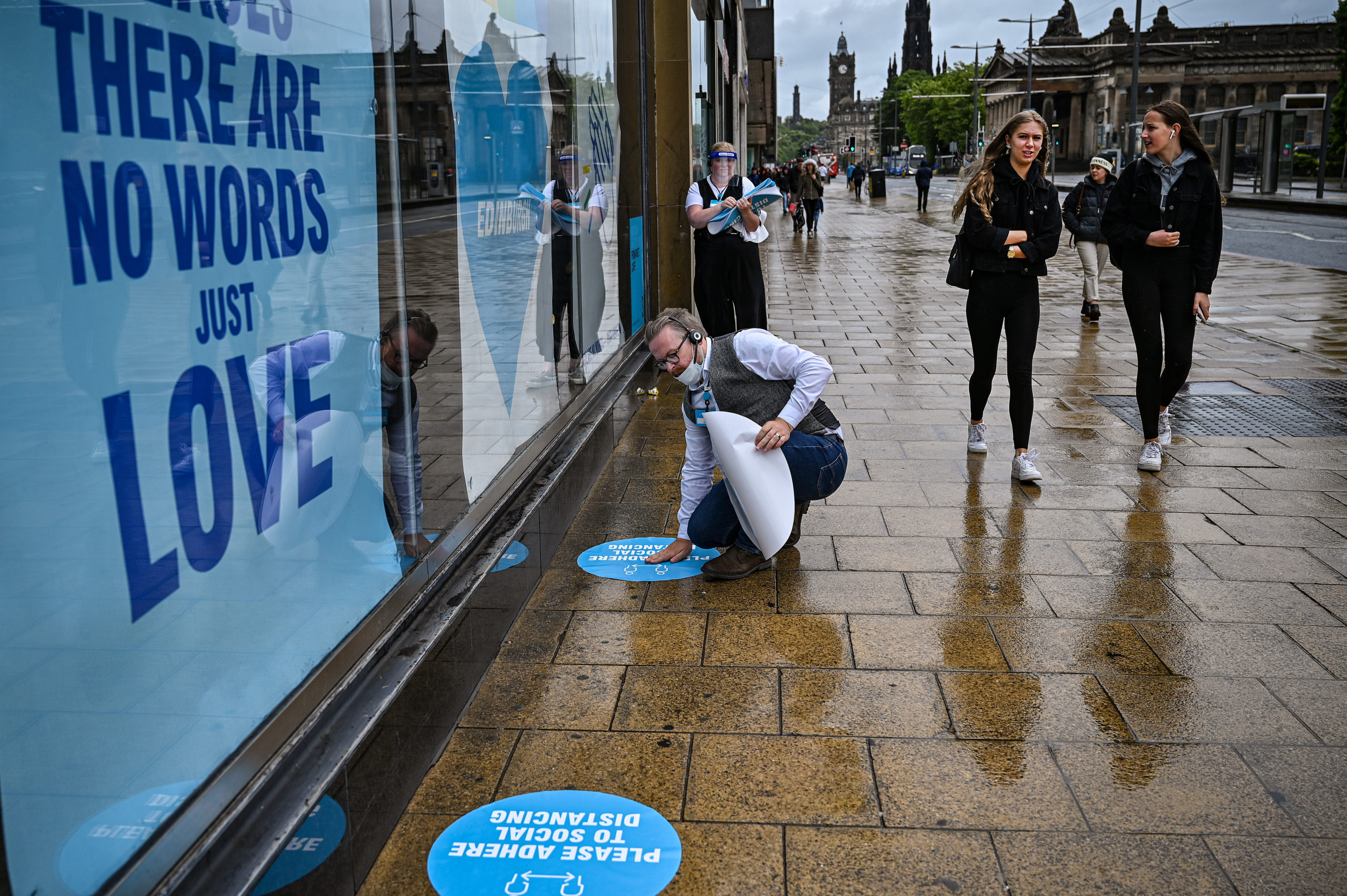 Staff apply social distancing signs to the ground while shoppers walk along Princes Street in Edinburgh.