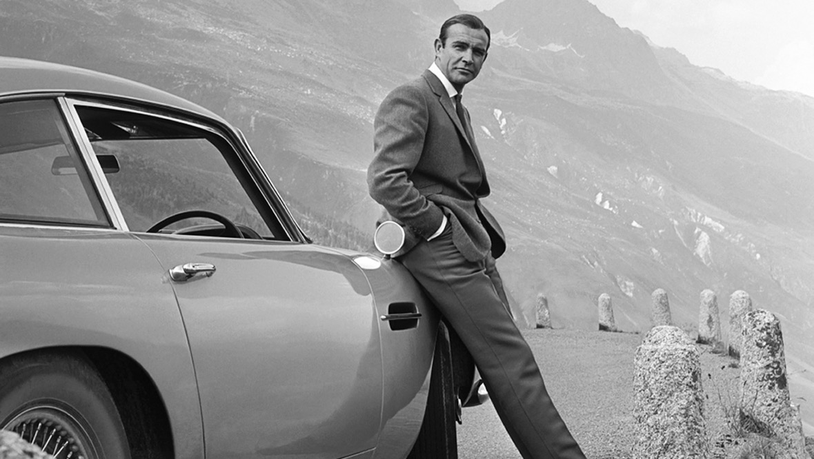 1964: Actor Sean Connery poses as James Bond next to his Aston Martin.