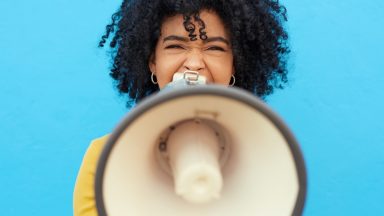 Cropped shot of a young woman holding a megaphone while posing against a blue background.