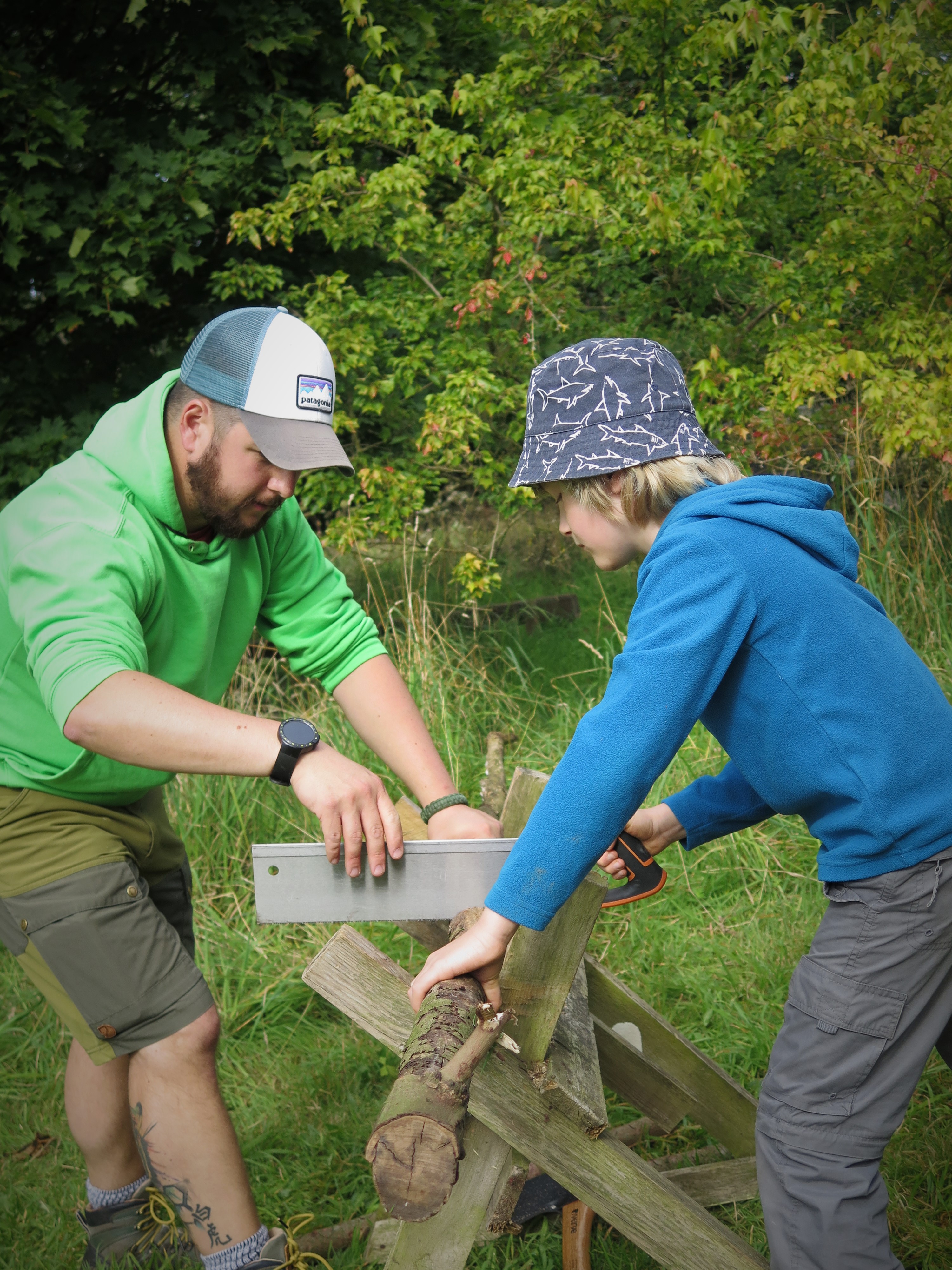 A forest school instructor teaches a child how to use a saw at Little Acorns CIC.