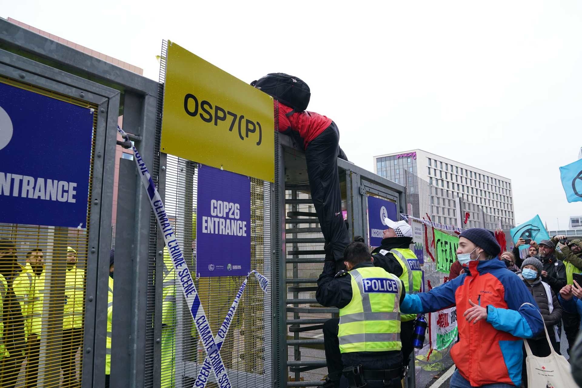 A protester tries to climb over the fence into COP26.
