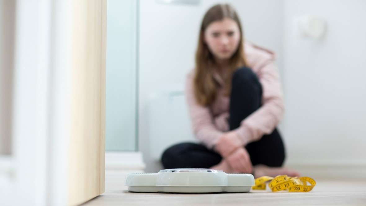 Stock image of teenager girl looking at scales and tape measure.