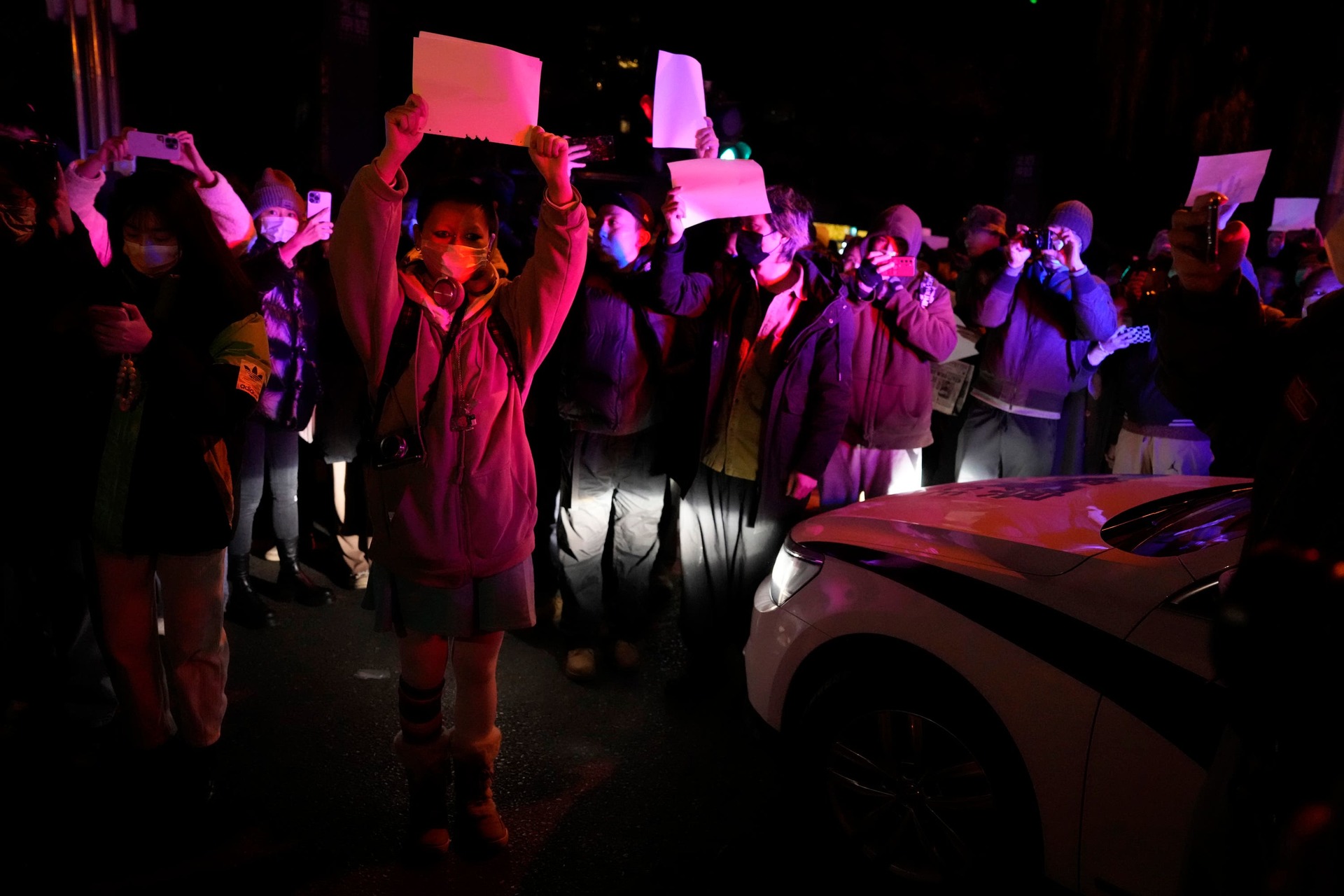 Protesters hold up blank papers and chant slogans as they march in protest in Beijing (AP)