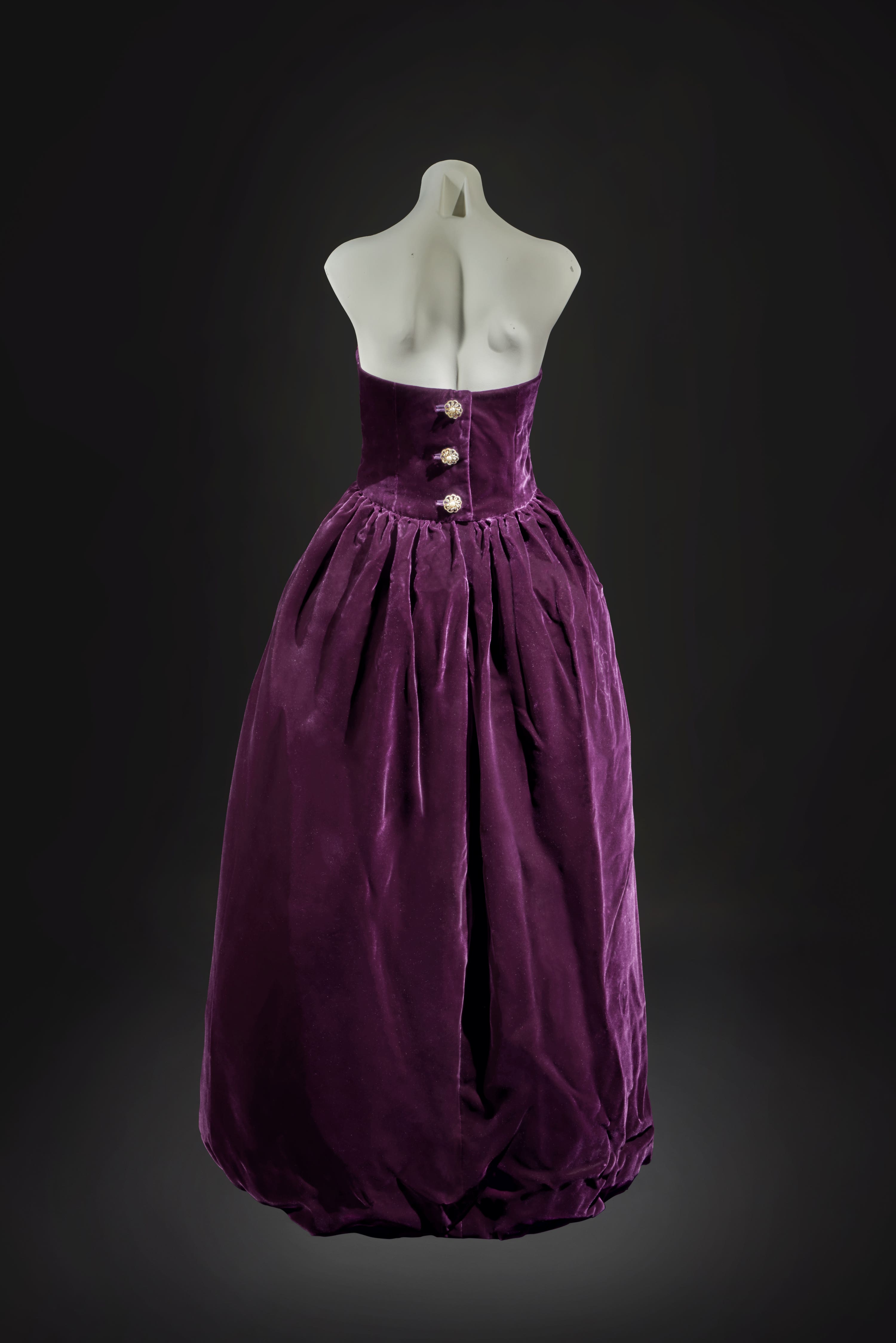 The ball dress is of deep aubergine silk velvet, with a tulip-shaped stiffened skirt, augmented by three paste buttons at the back. 