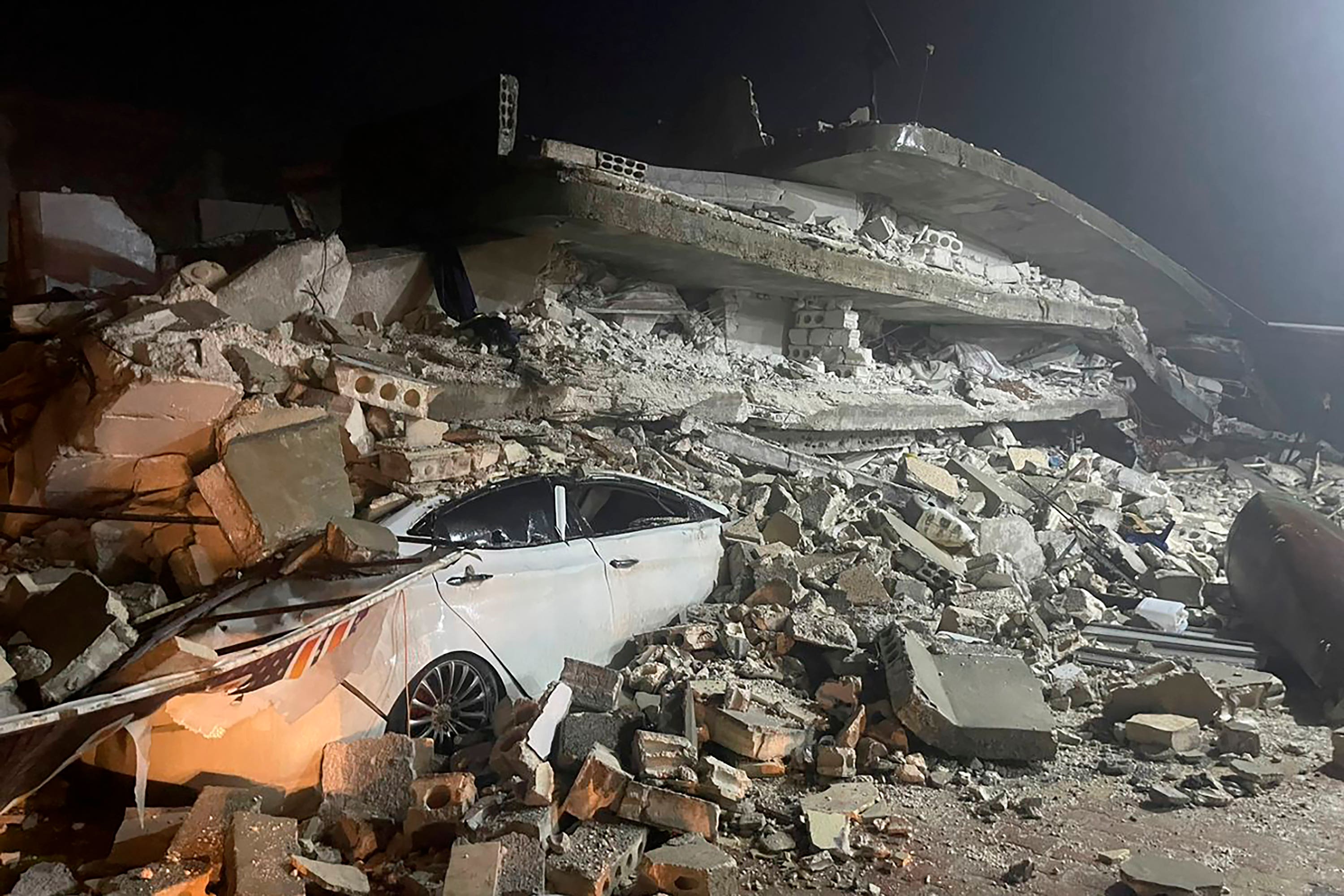 A car is seen under the wreckage of a collapsed building, in Azmarin town, in Idlib province, northern Syria (AP)

