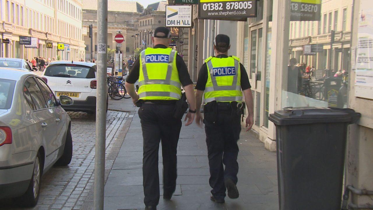 Two police officers are seen walking down a street