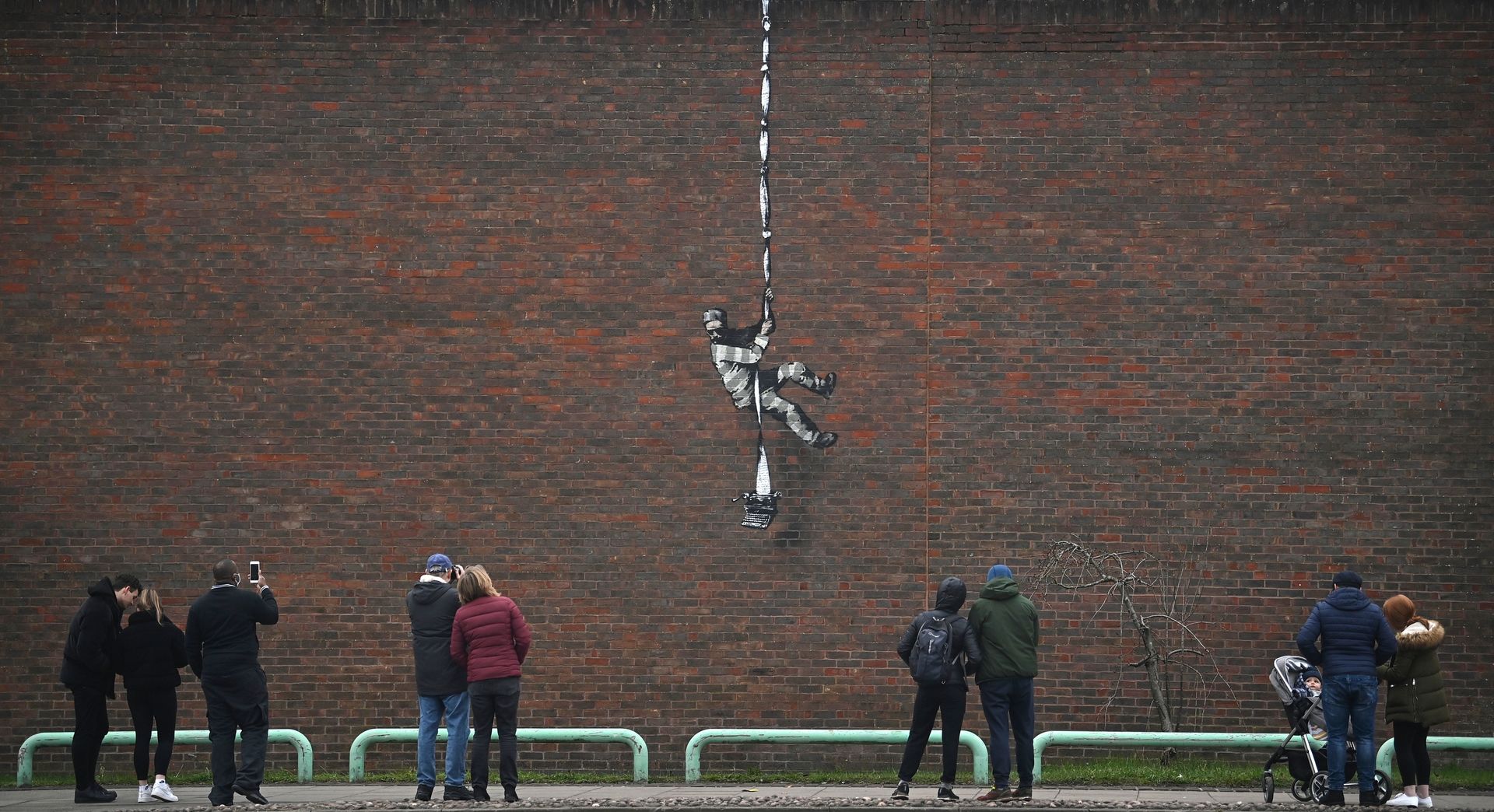 Members of the public pause to look at an artwork bearing the hallmarks of street artist Banksy on the side of Reading Prison in Reading.
