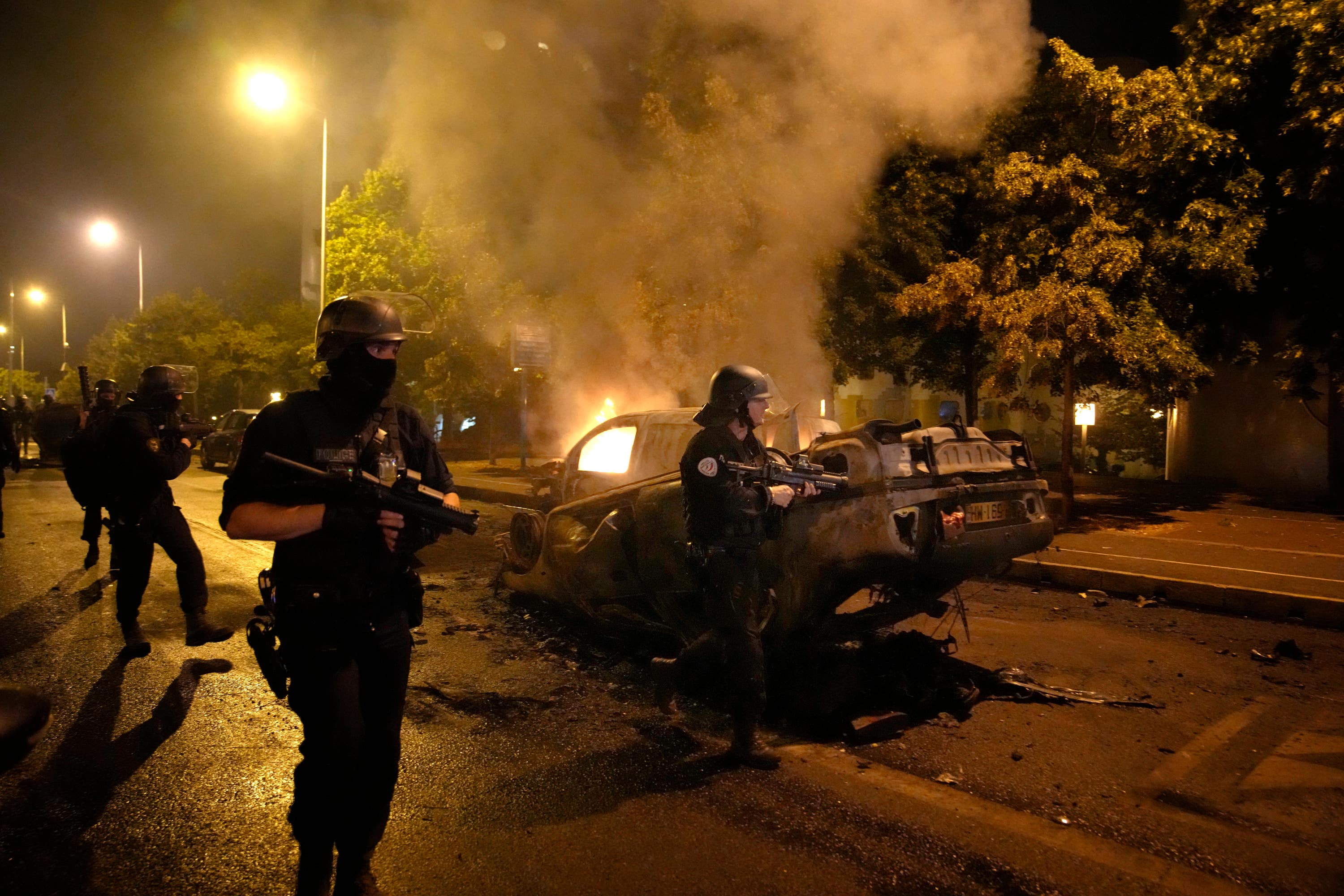 Police officers walk past burned cars as they clash with youths in Nanterre.