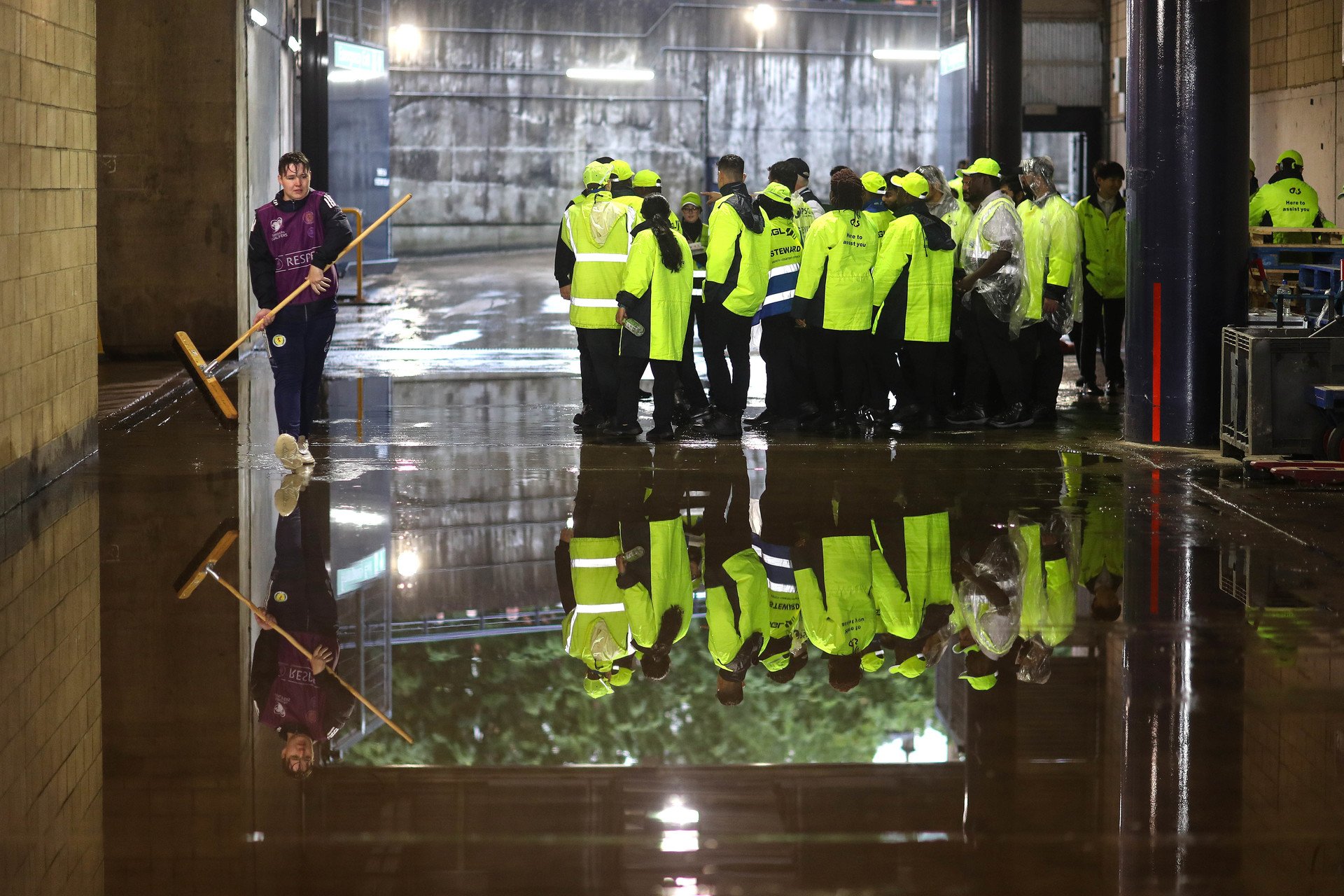 A soaking wet ballboy walks through a flooded concourse at Hampden Park as stewards stand by.