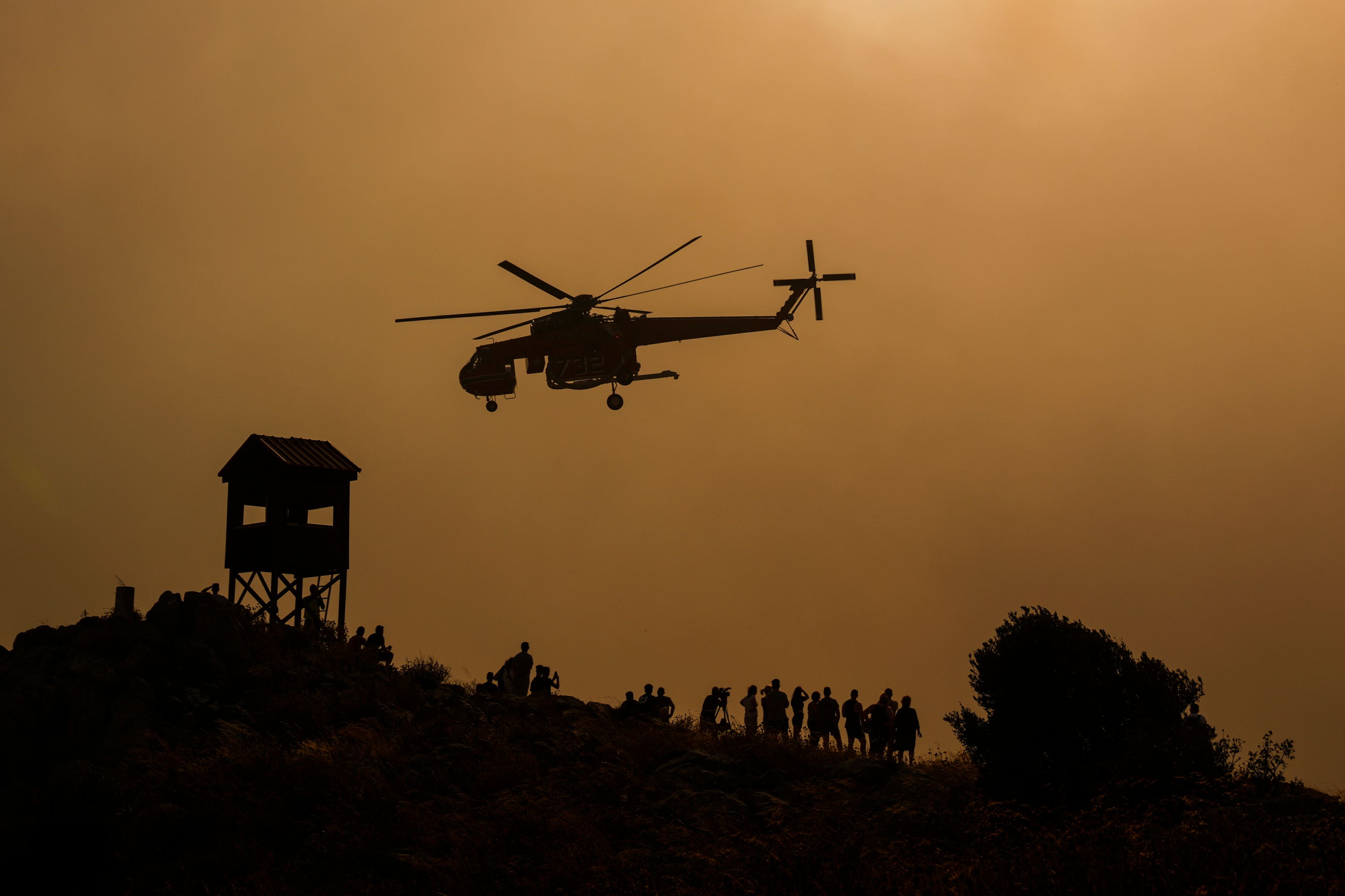 A firefighting helicopter dumps water on a wildifre (Petros Giannakouris/AP) 