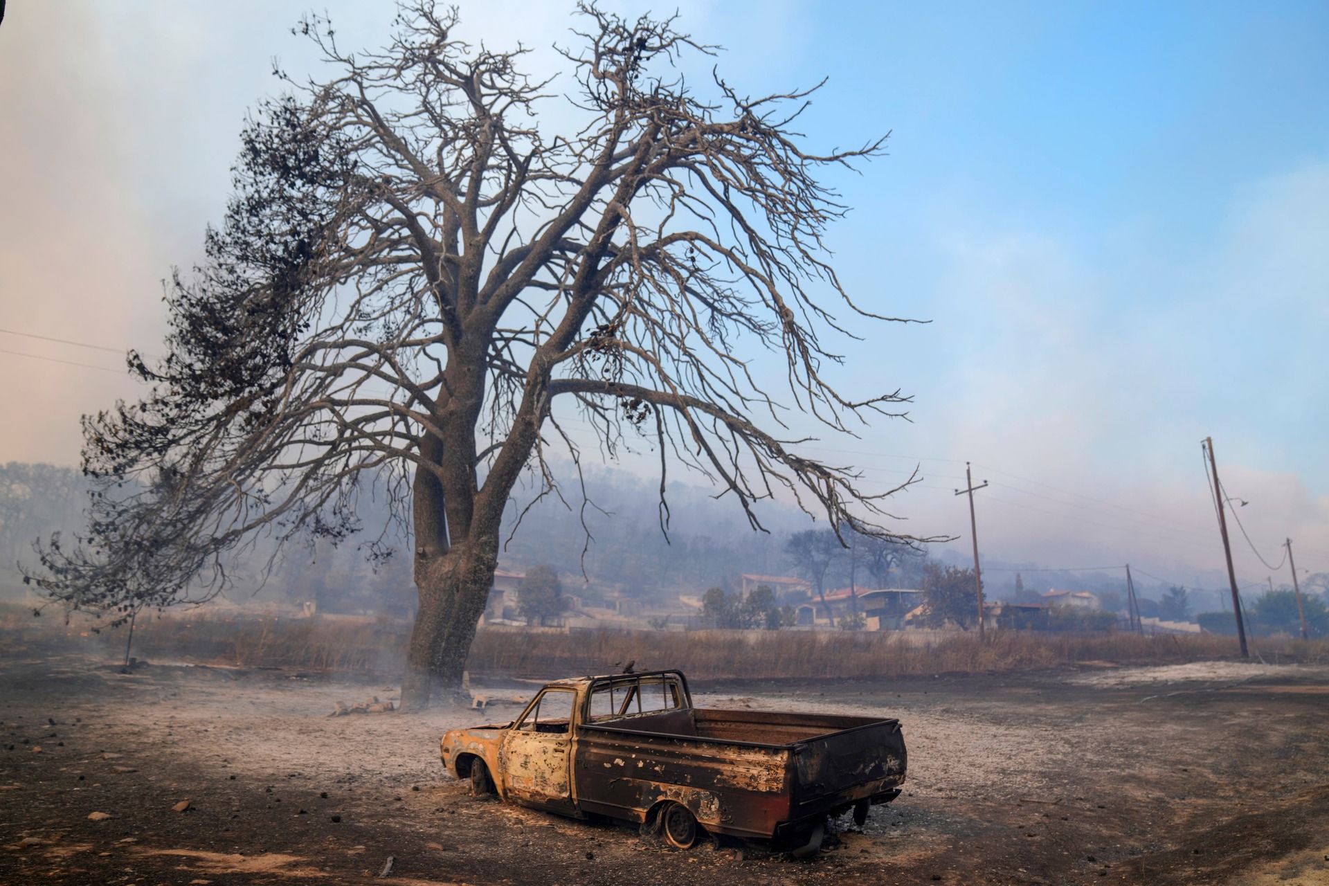 A damaged car stands in front of a burned tree near Loutraki west of Athens (Petros Giannakouris/AP)
