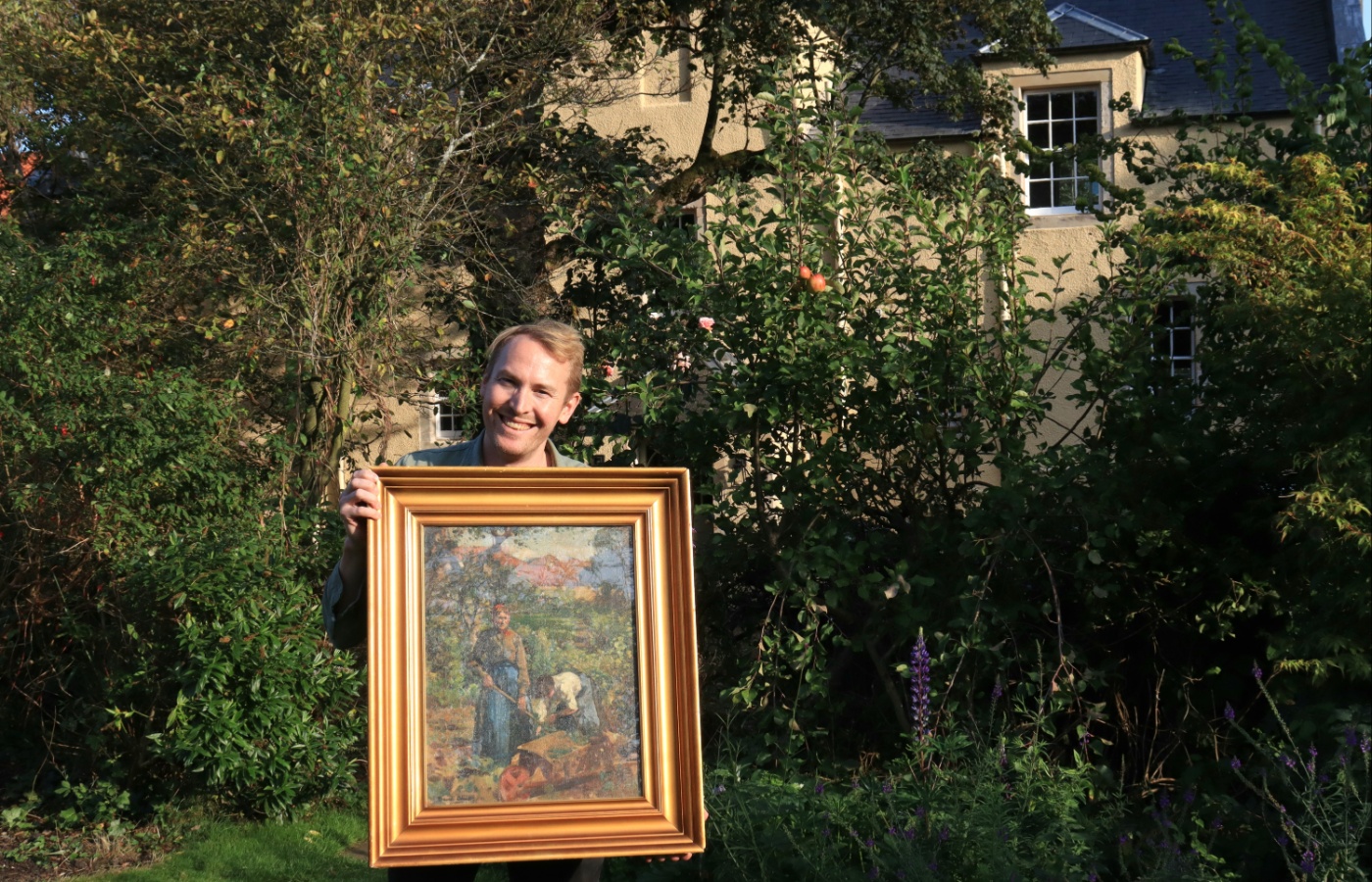 Orchard Croft owner Matt Kirkbride poses with a painting from David Alison in the garden where it was painted.