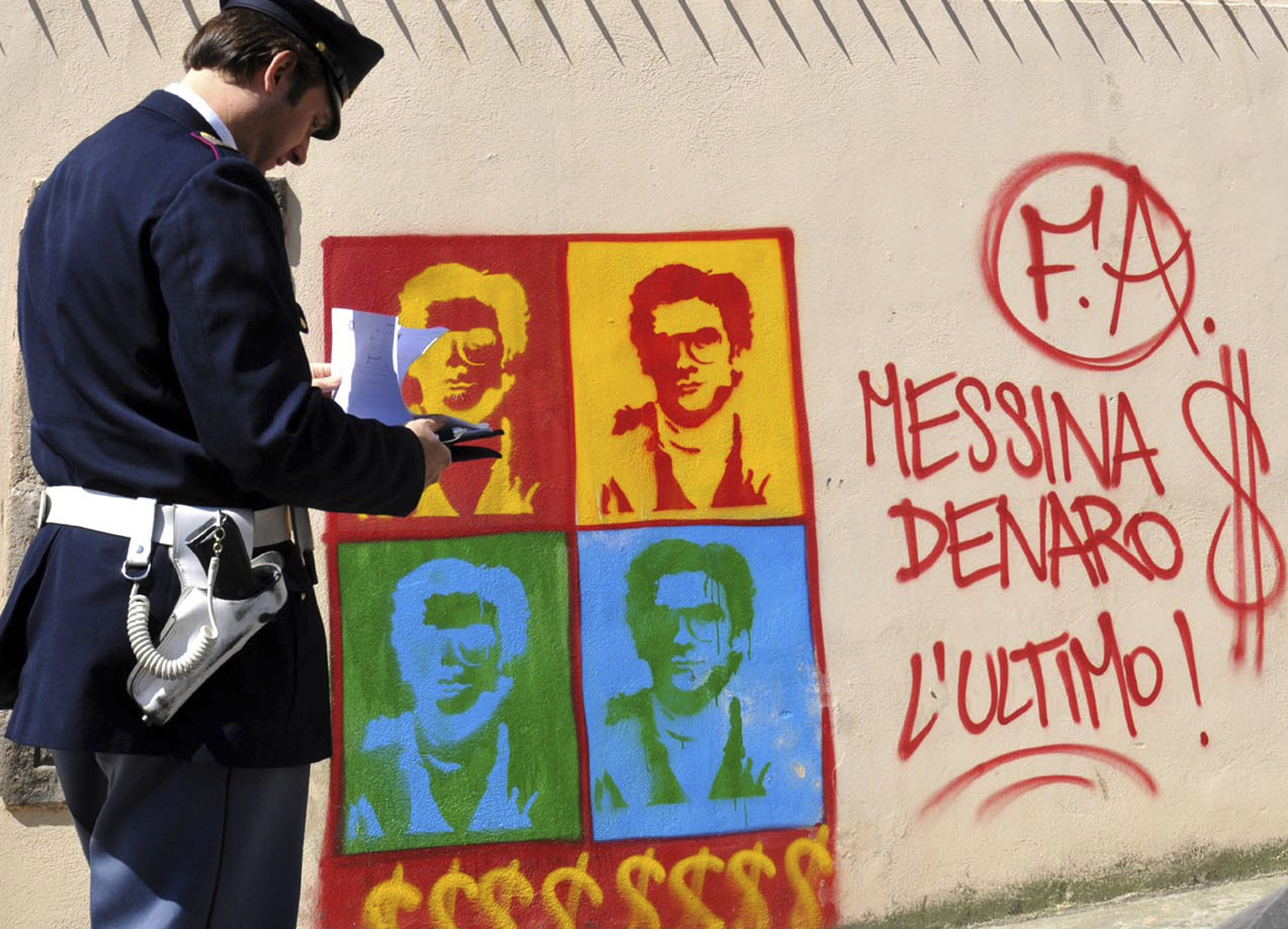 An Italian police officer looks at graffiti, on the perimeter wall of Palermo’s city’s cathedral, portraying Messina Denaro.