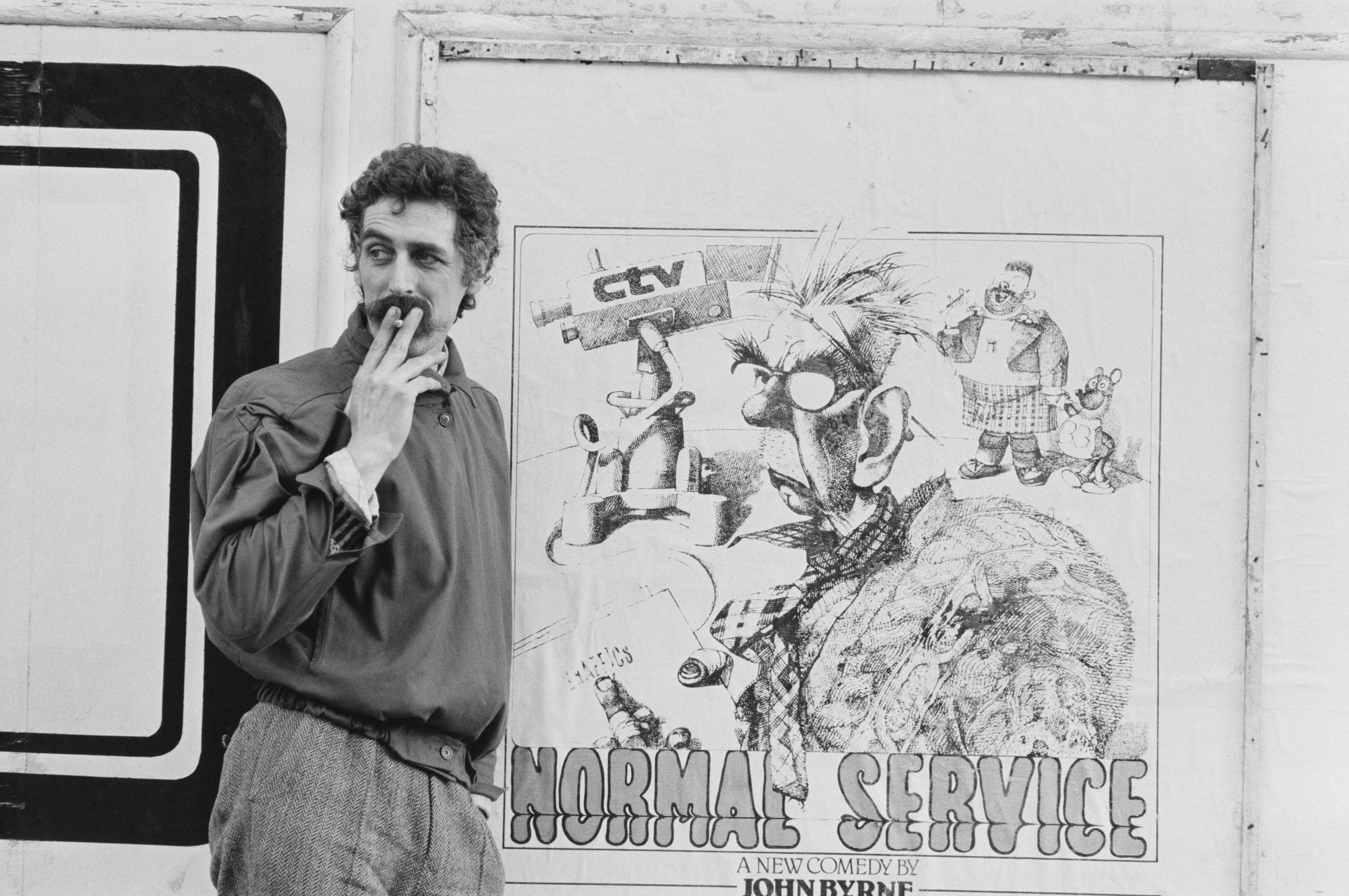 Scottish playwright and artist John Byrne near a poster promoting his comedy 'Normal Service', UK, March 9, 1979.