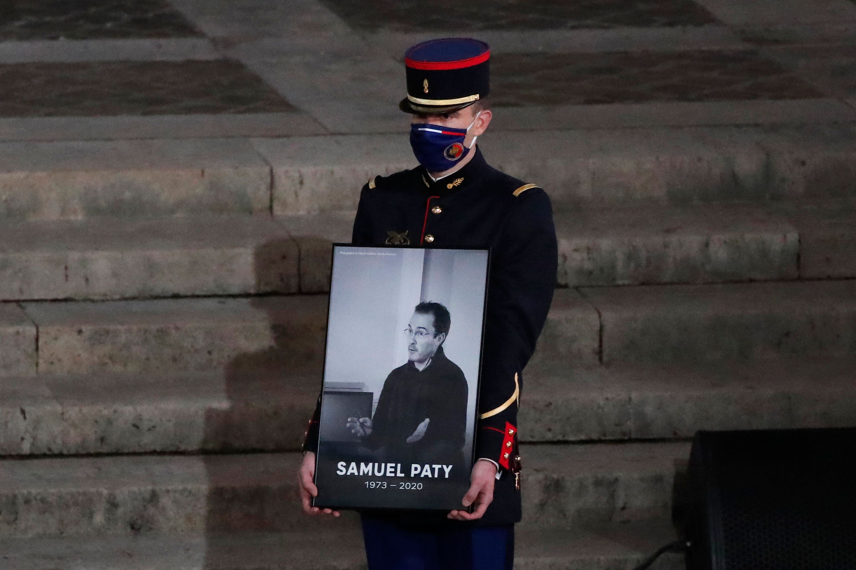 A Republican Guard holds a portrait of Samuel Paty in the courtyard of the Sorbonne university during a national memorial event (Francois Mori, Pool/AP) 