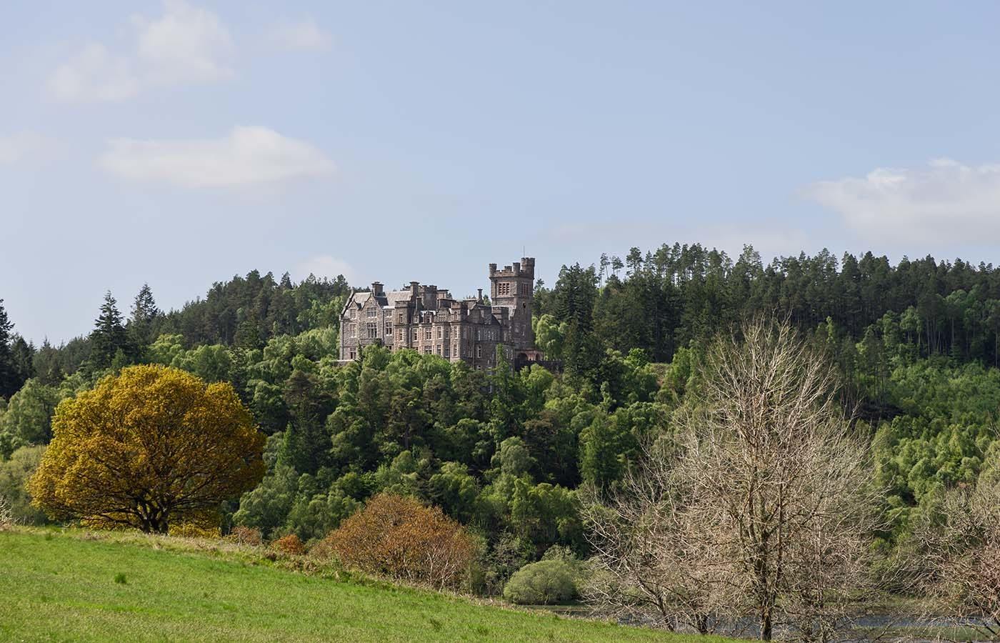 Nestled among lush forests in the Scottish Highlands, Carbisdale Castle, overlooking a serene landscape marked by vibrant greenery and a tranquil river