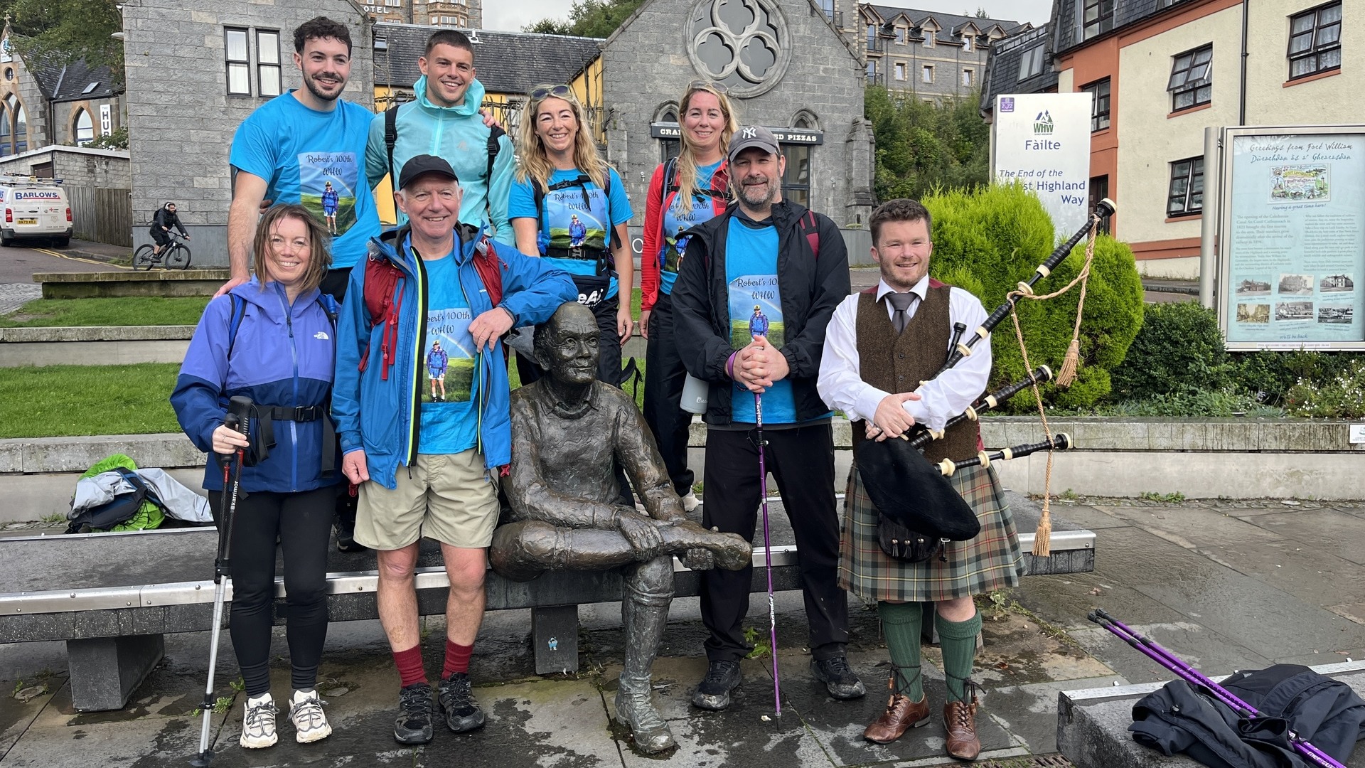 Robert Marshall at the ‘Man with Sore Feet’ statue at the end of the West Highland Way at Fort William with his six children and The Munro Bagpiper, who piped them across the finish line.