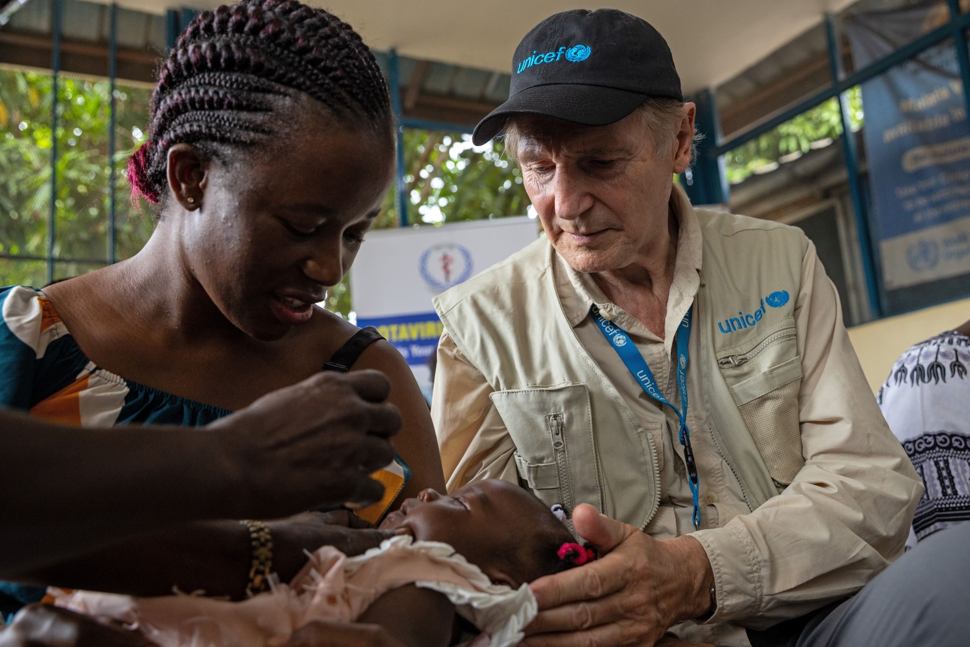 Liam Neeson sits with Josephine Mitaindure as her three-month-old daughter, Eliana Asiaka is vaccinated against polio (Unicef/PA).