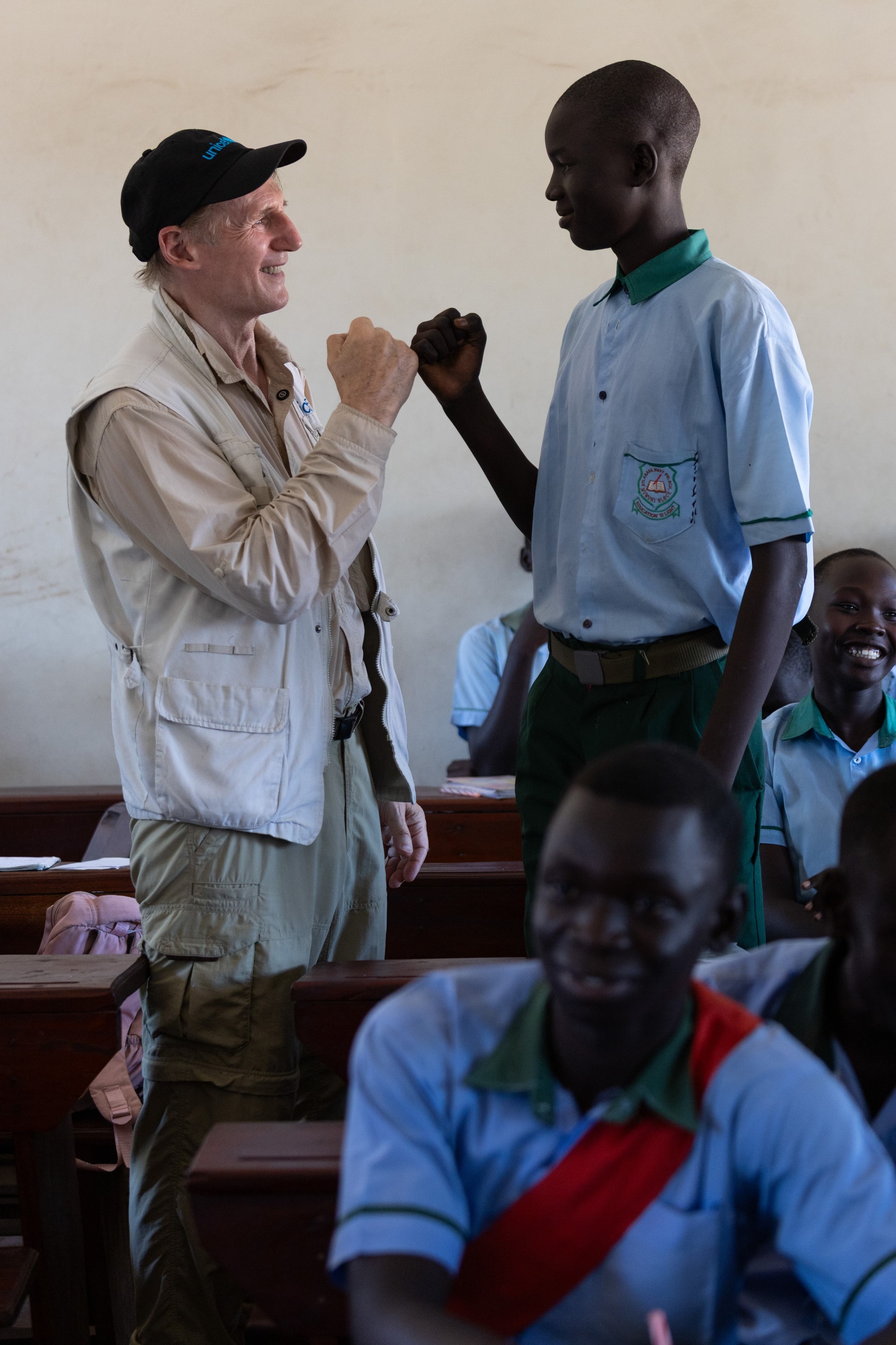 Liam Neeson bumps fists with John Juda, 19, while visiting students in the Primary 8 class at the Unicef-supported Atlabara West Primary School in Juba (Unicef/PA).