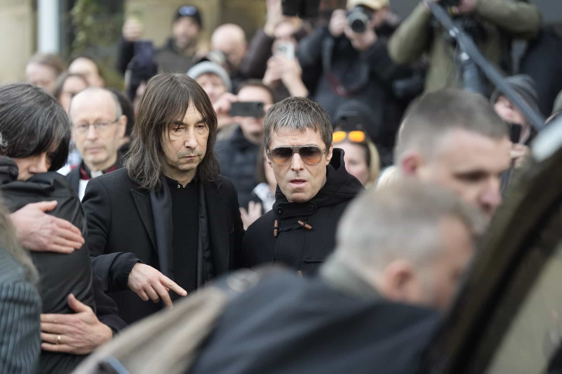 Bobby Gillespie (left) and Liam Gallagher watch as the coffin is placed in the back of the hearse after the funeral service