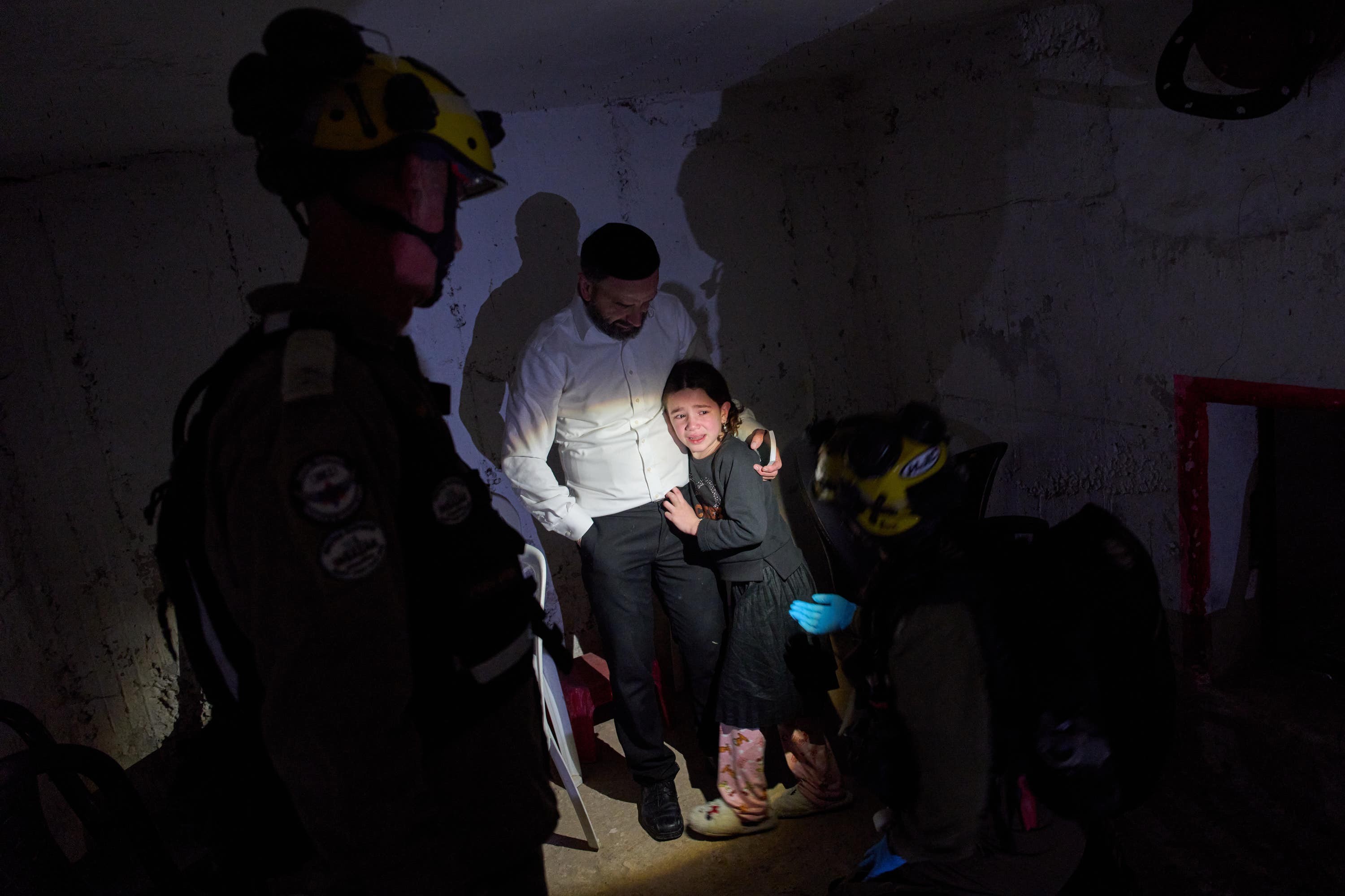 A young girl is comforted by her father and Israeli soldiers as they take cover in a bomb shelter during air raid sirens warning of incoming Iranian missile strikes in Bnei Brak