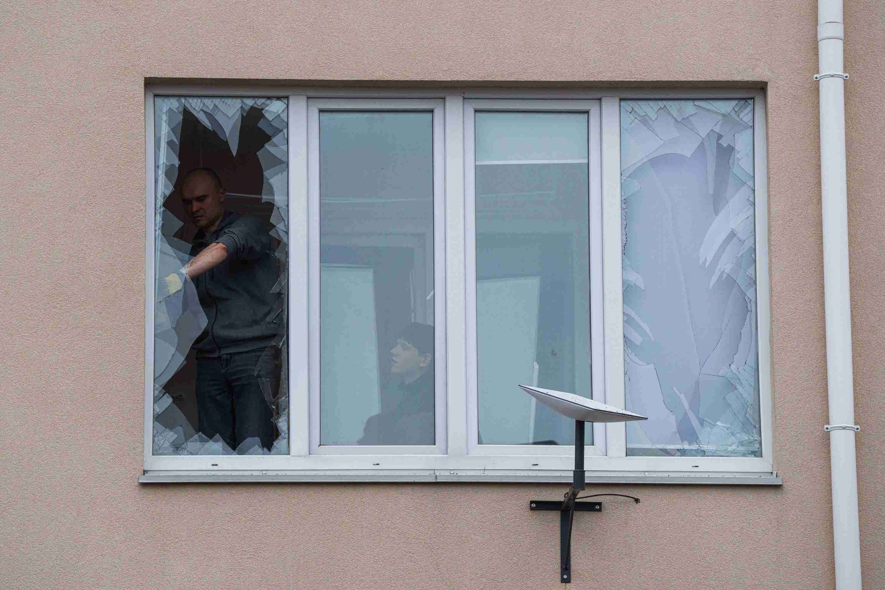 People remove broken glass from their windows after a Russian strike on a residential neighbourhood in Kriukivshchyna, near Kyiv